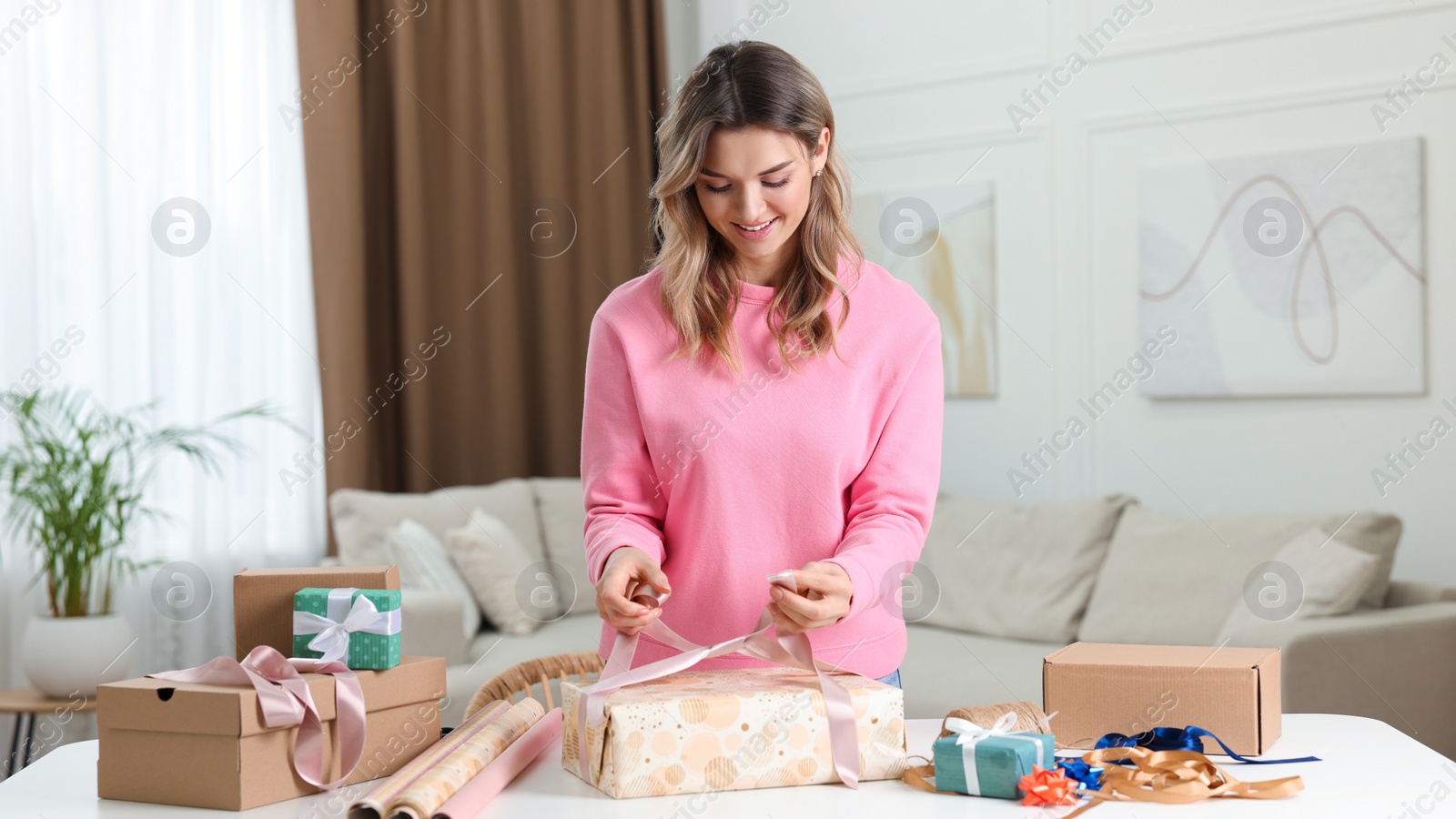 Photo of Beautiful young woman wrapping gift at table in living room