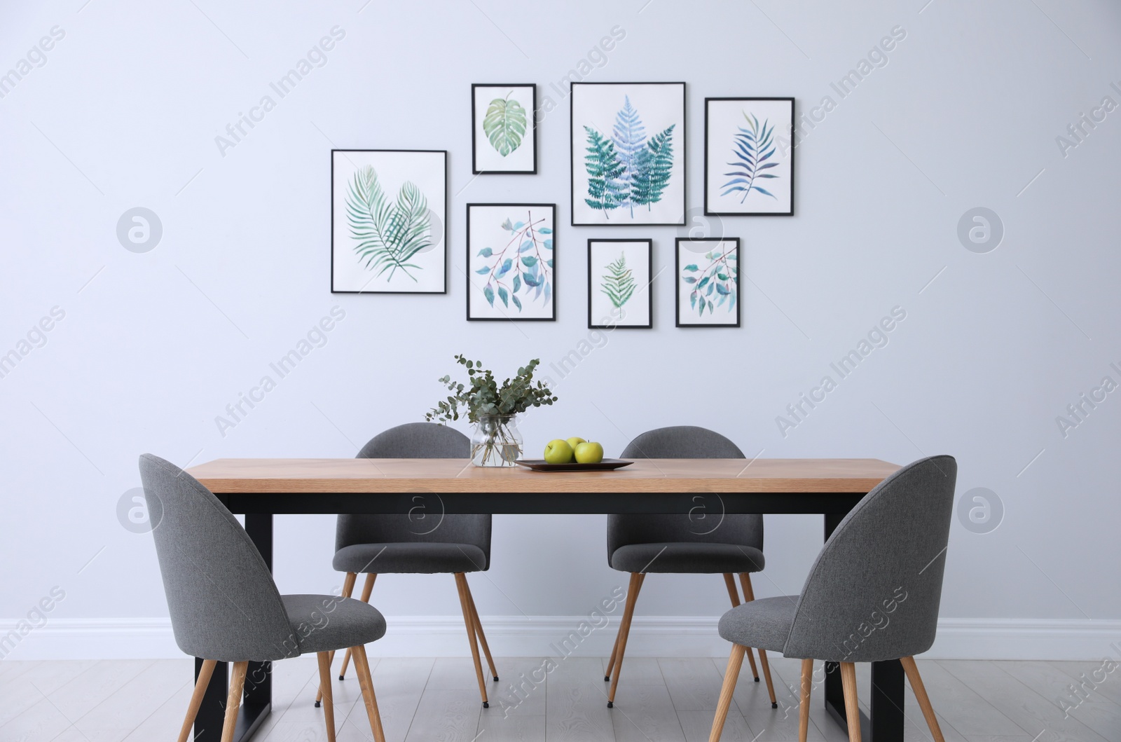 Photo of Stylish room interior with modern table, chairs and paintings of tropical leaves. Idea for design