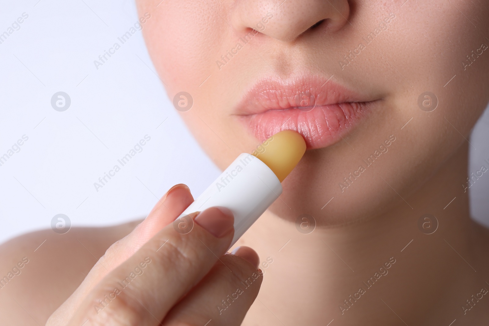 Photo of Woman applying hygienic lipstick on lips against white background, closeup