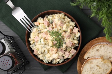 Photo of Tasty Olivier salad with boiled sausage in bowl served on grey wooden table, flat lay