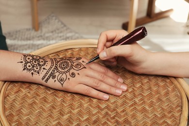 Photo of Master making henna tattoo on hand at table, closeup. Traditional mehndi