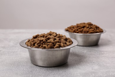 Photo of Dry food in pet bowls on grey surface