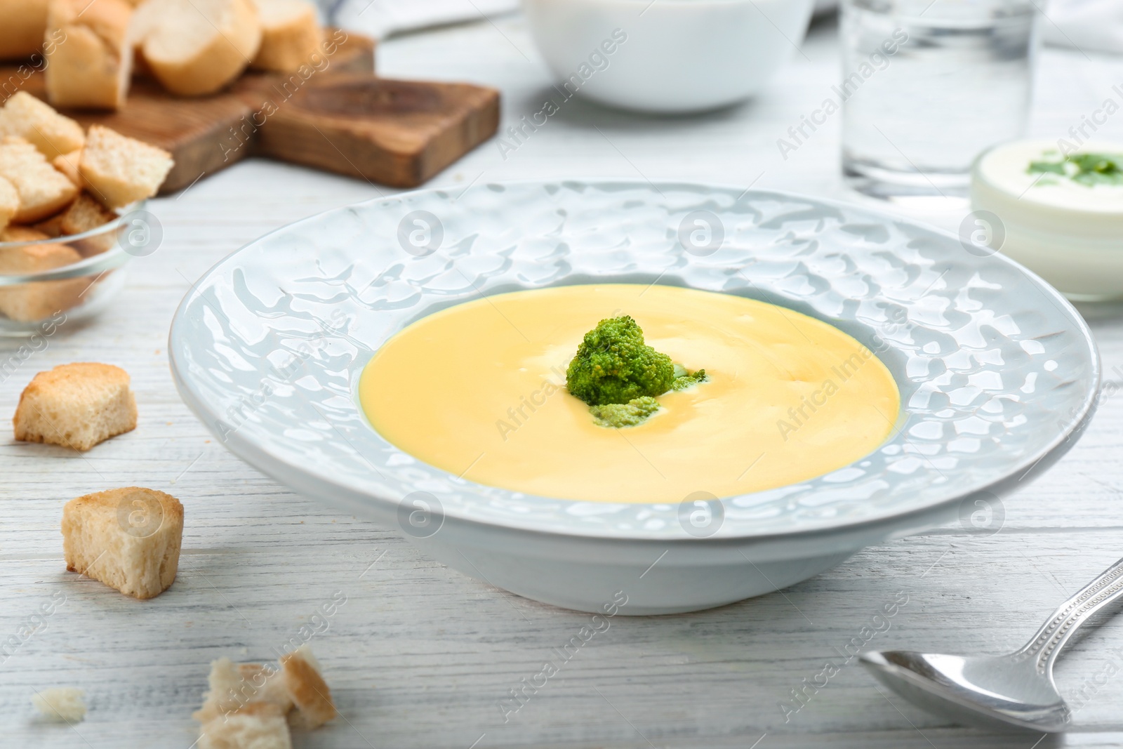 Photo of Bowl of cheese cream soup with broccoli served on white wooden table