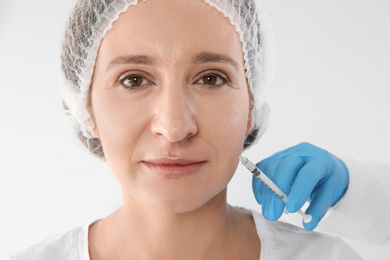 Photo of Mature woman getting facial injection on white background. Cosmetic surgery concept