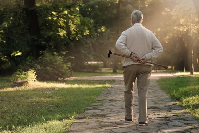 Photo of Senior man with walking cane in park, back view. Space for text