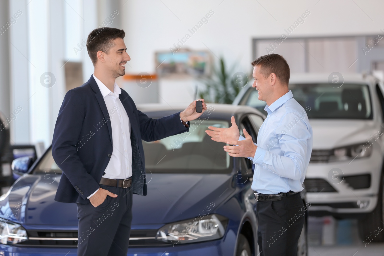 Photo of Young salesman working with client in car dealership