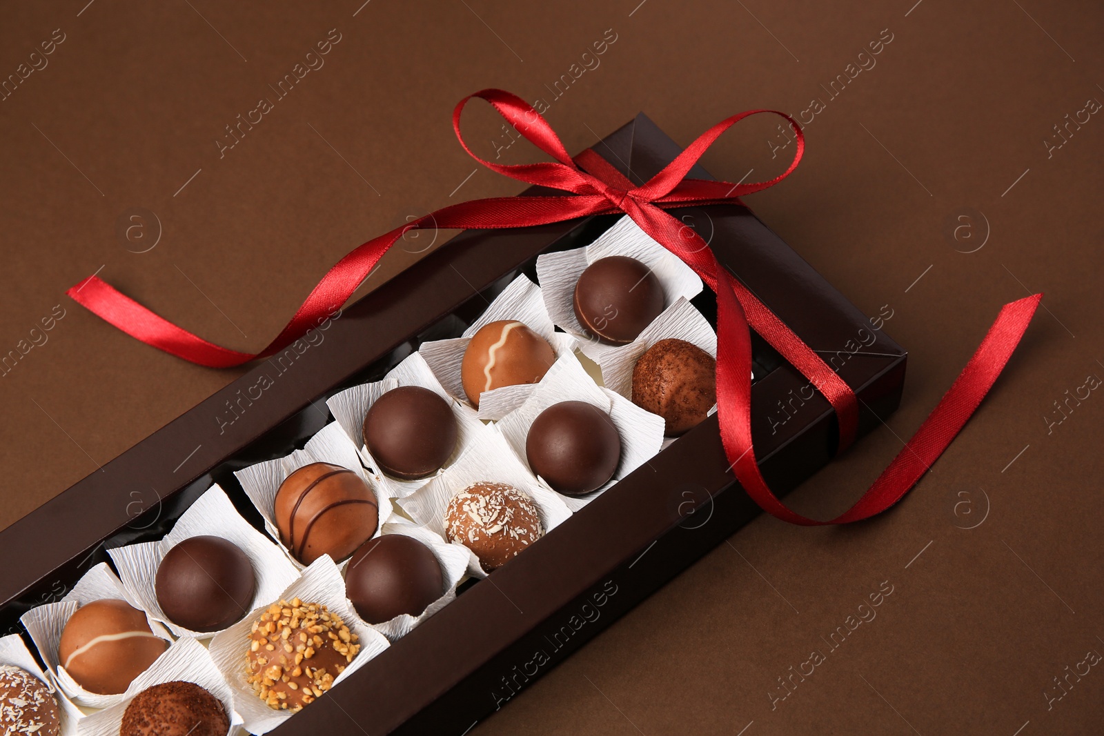 Photo of Box with delicious chocolate candies on brown table, closeup