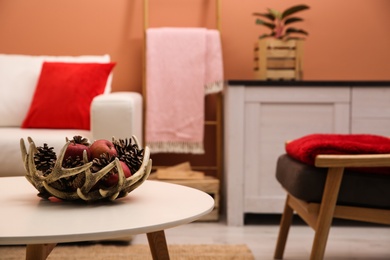 Photo of Decorative antler bowl with apples and pine cones in living room interior inspired by autumn colors