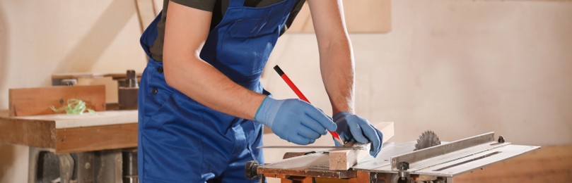 Image of Professional carpenter making mark on wooden bar in workshop, closeup. Banner design