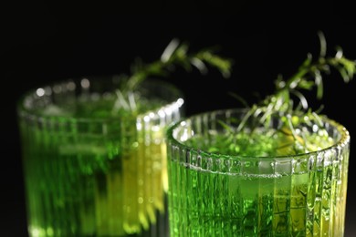 Photo of Glasses of homemade refreshing tarragon drink on black background, closeup