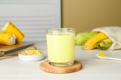 Photo of Tasty fresh corn milk in glass and cobs on white wooden table