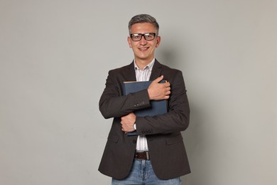 Teacher in glasses holding notebooks on grey background