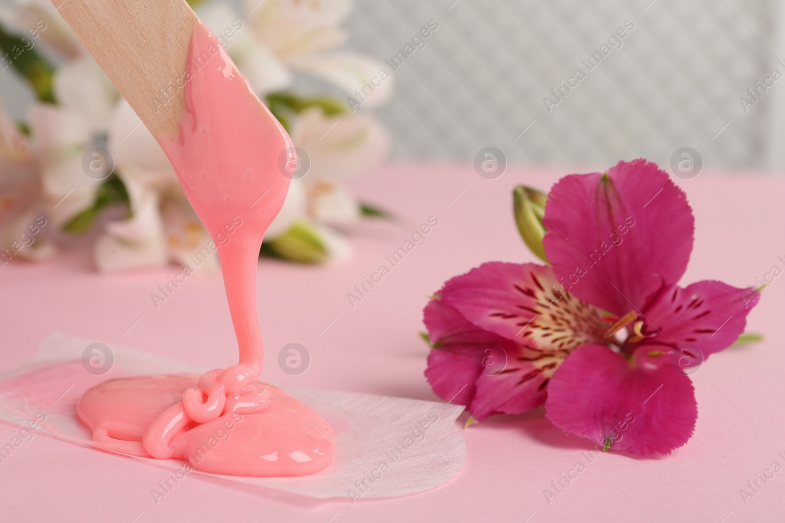 Photo of Wooden spatula with hot depilatory wax and flower on light pink table, closeup