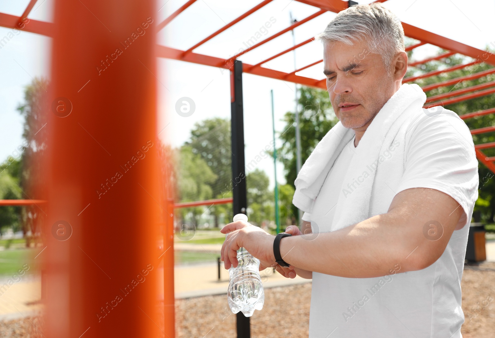 Photo of Handsome mature man looking at fitness tracker on sports ground. Healthy lifestyle