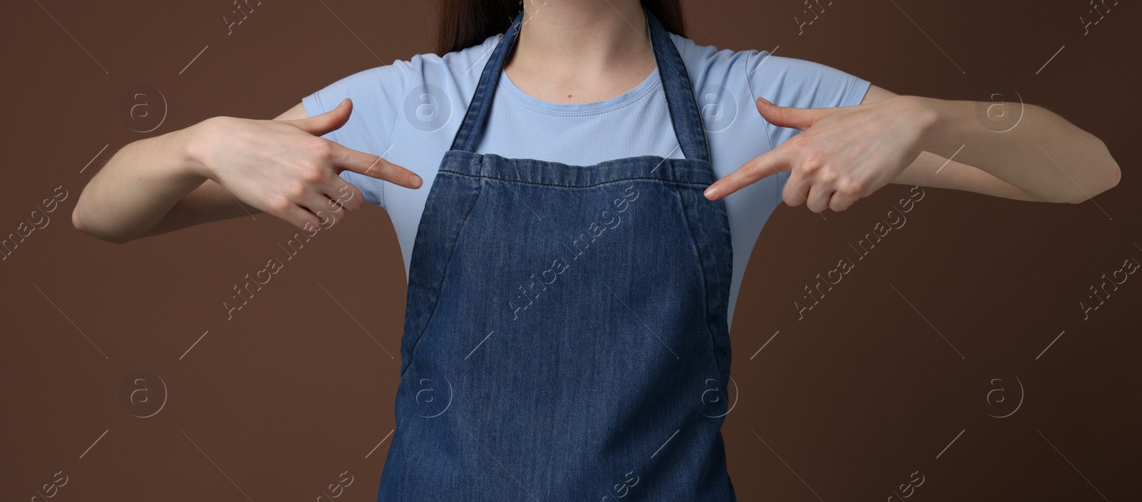 Photo of Woman pointing at kitchen apron on brown background, closeup. Mockup for design