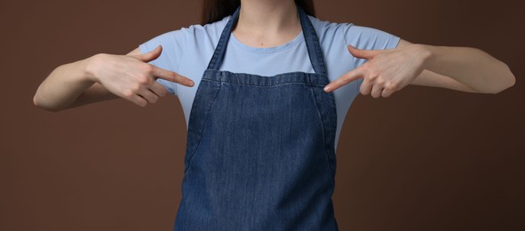 Photo of Woman pointing at kitchen apron on brown background, closeup. Mockup for design