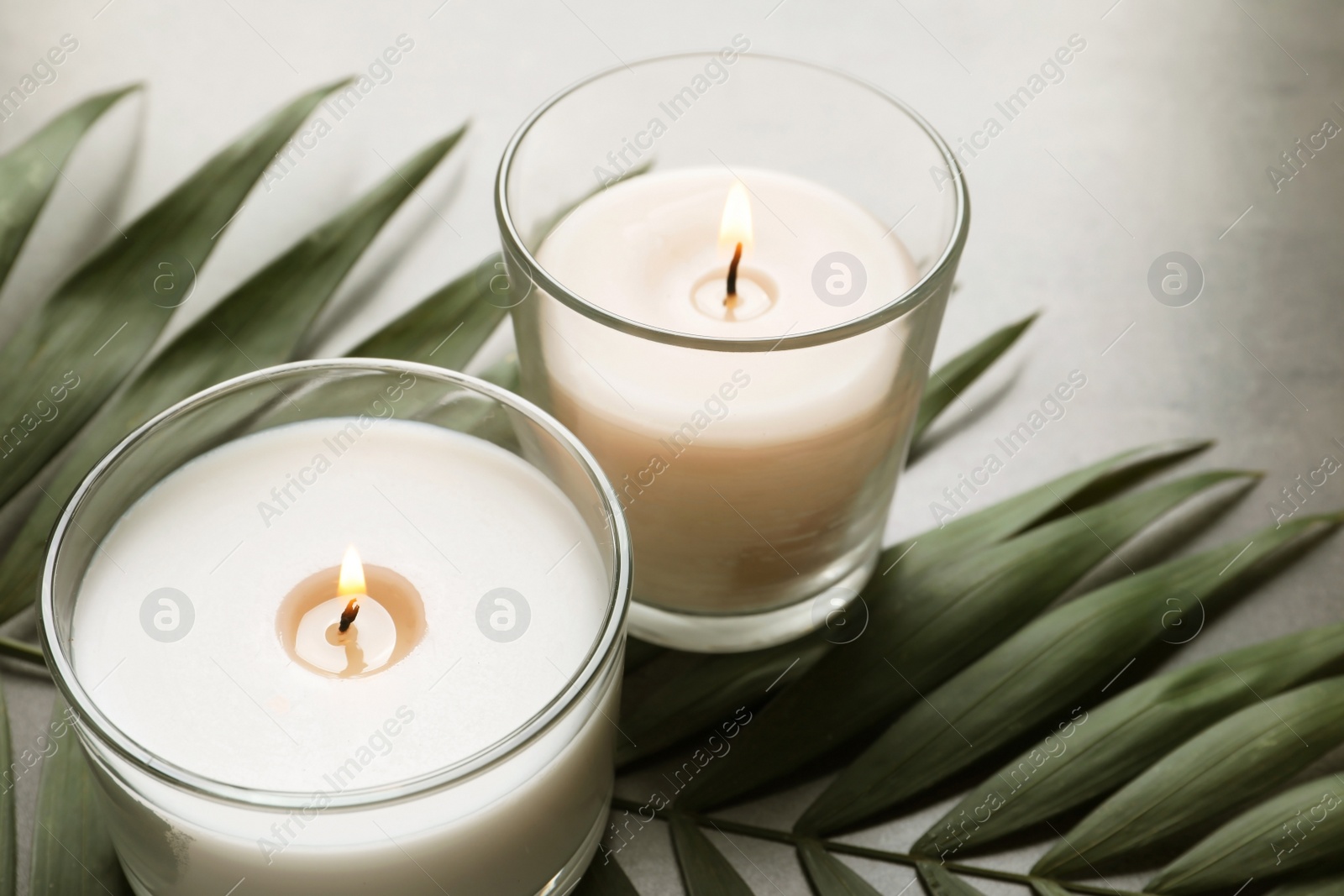 Photo of Burning wax candles and tropic leaf on table