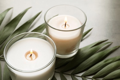 Burning wax candles and tropic leaf on table