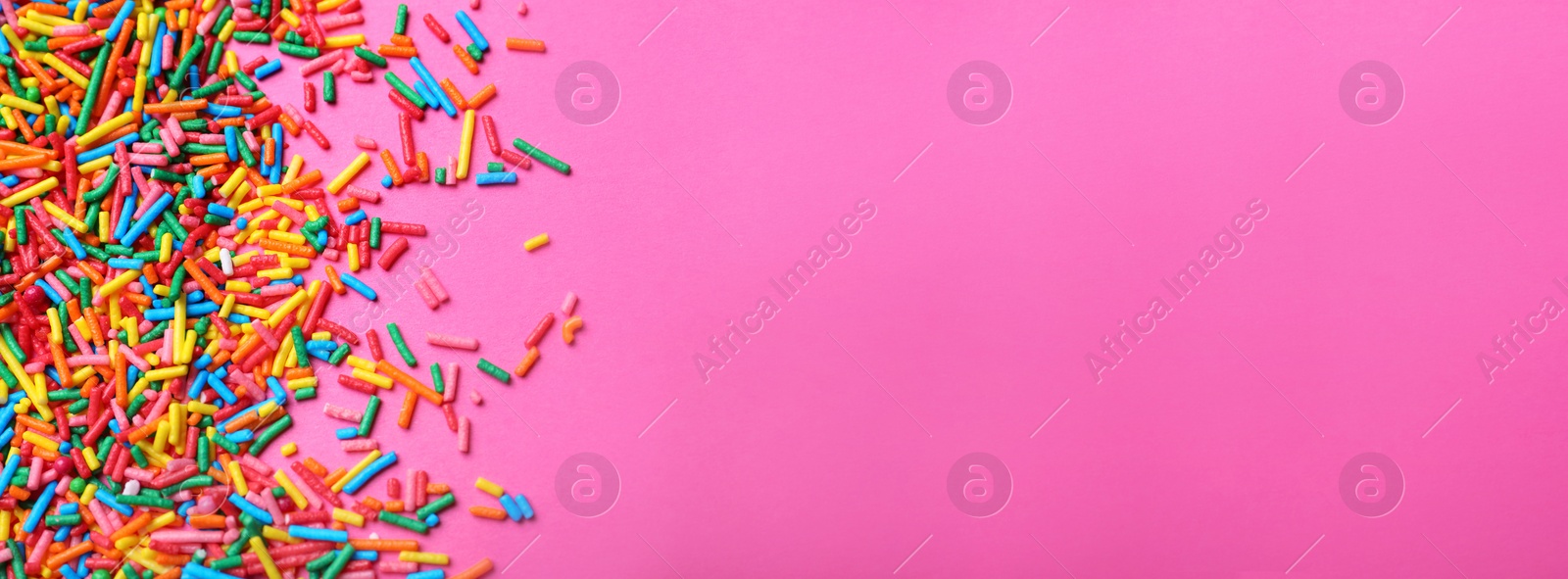 Photo of Bright colorful sprinkles on pink background, flat lay with space for text. Confectionery decor