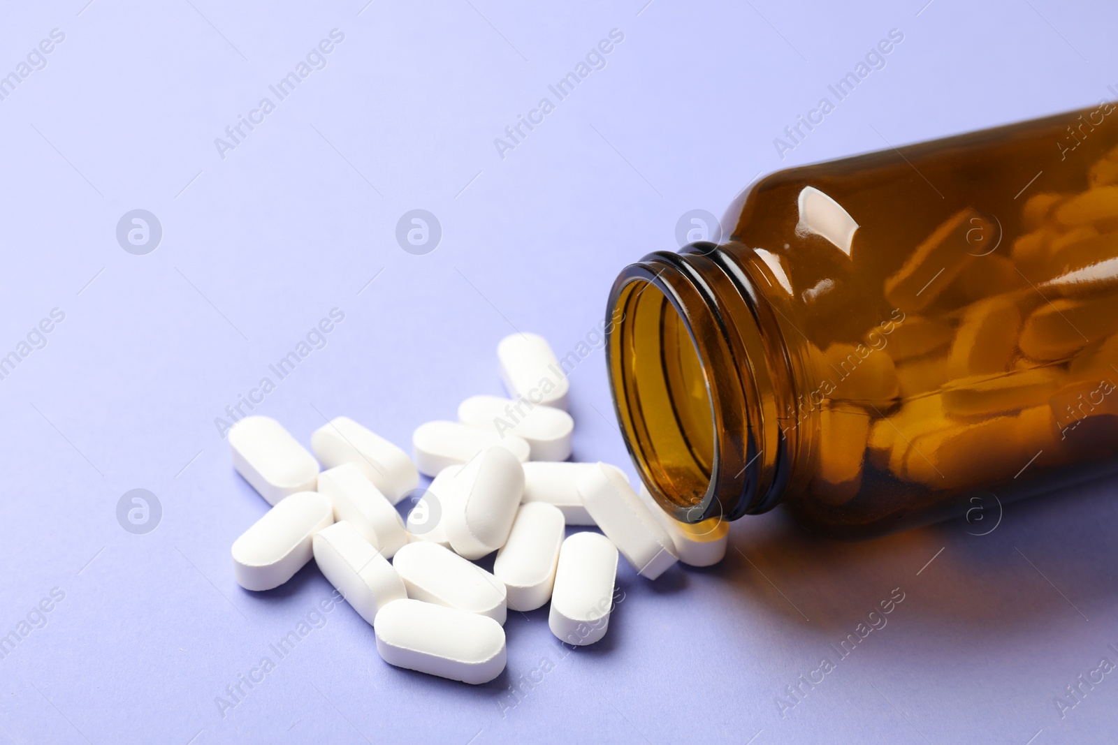 Photo of Bottle and vitamin capsules on violet background, closeup