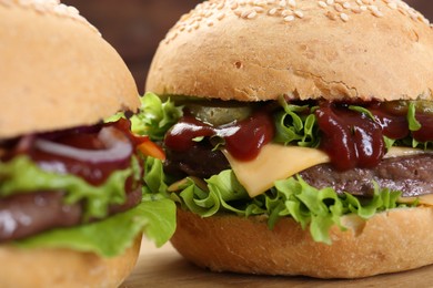 Photo of Delicious cheeseburgers with lettuce, pickle, ketchup and patty on table, closeup