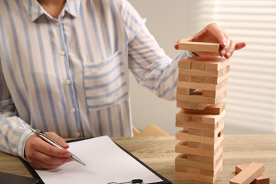 Photo of Playing Jenga. Woman building tower with blocks at wooden table in office, closeup