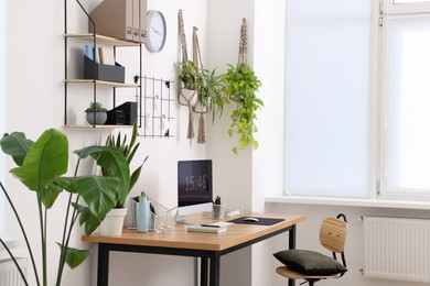 Cozy workplace with computer, modern furniture and houseplants at home