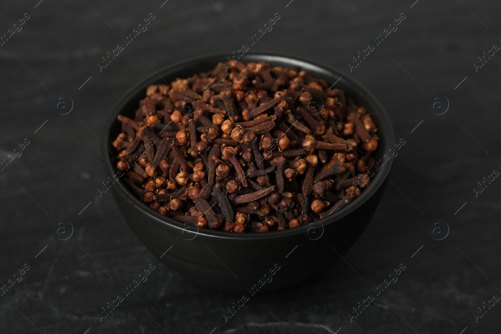 Photo of Bowl of aromatic dry cloves on black table