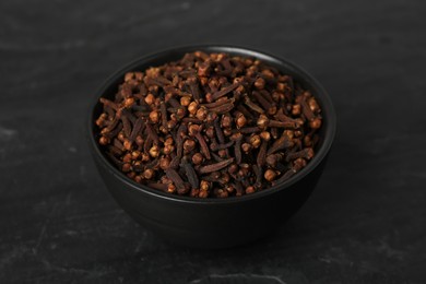 Photo of Bowl of aromatic dry cloves on black table