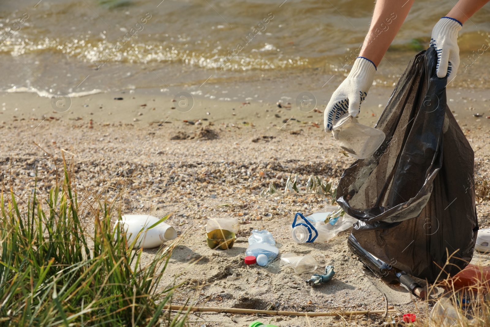 Photo of Woman in gloves with trash bag collecting garbage on beach, closeup