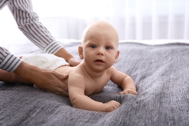 Young woman massaging cute little baby on bed at home