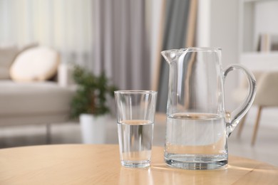 Jug and glass with clear water on table indoors, closeup. Space for text