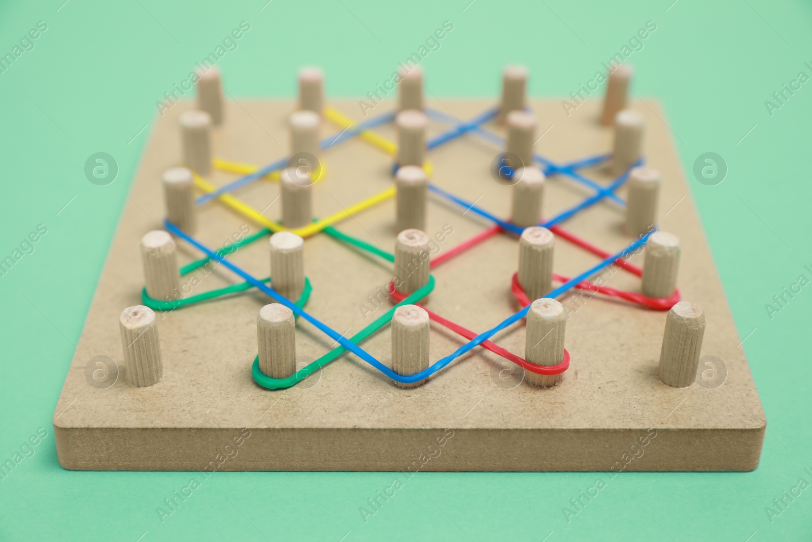 Photo of Wooden geoboard with rubber bands on green background, closeup. Educational toy for motor skills development