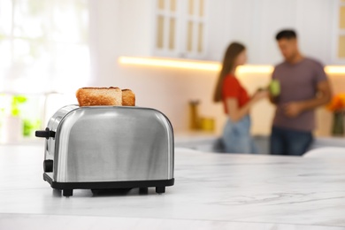 Photo of Modern toaster with slices of bread and blurred couple on background