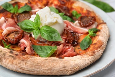 Photo of Delicious pizza with burrata cheese, basil, ham and sun-dried tomatoes on plate, closeup