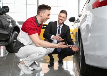 Photo of Salesman consulting young man at dealership. Buying new car