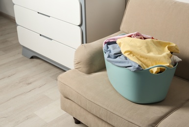 Photo of Laundry basket with dirty clothes on sofa indoors. Space for text