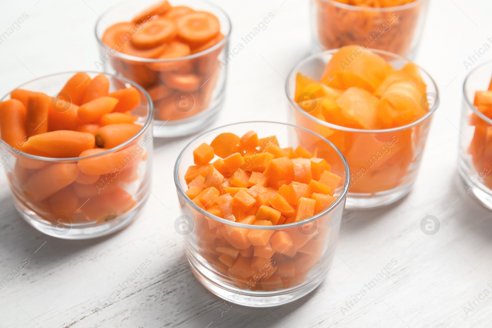 Photo of Glasses with cut carrots on wooden background