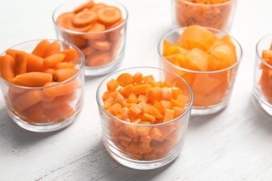 Photo of Glasses with cut carrots on wooden background