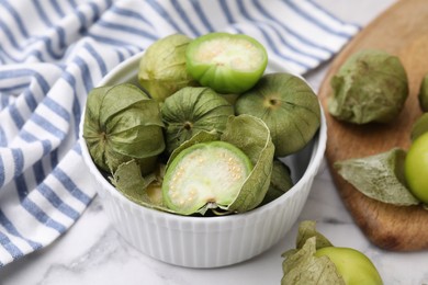 Photo of Fresh green tomatillos with husk in bowl on light table, closeup
