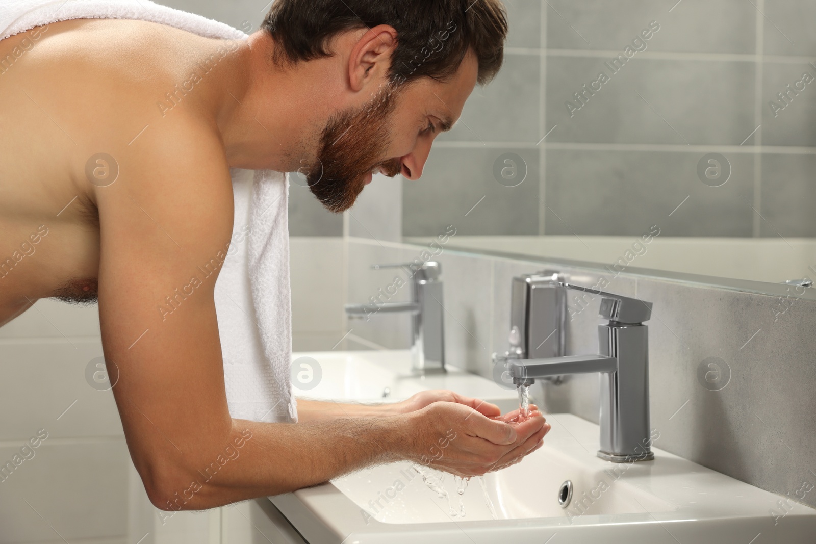 Photo of Handsome man washing face in bathroom, closeup