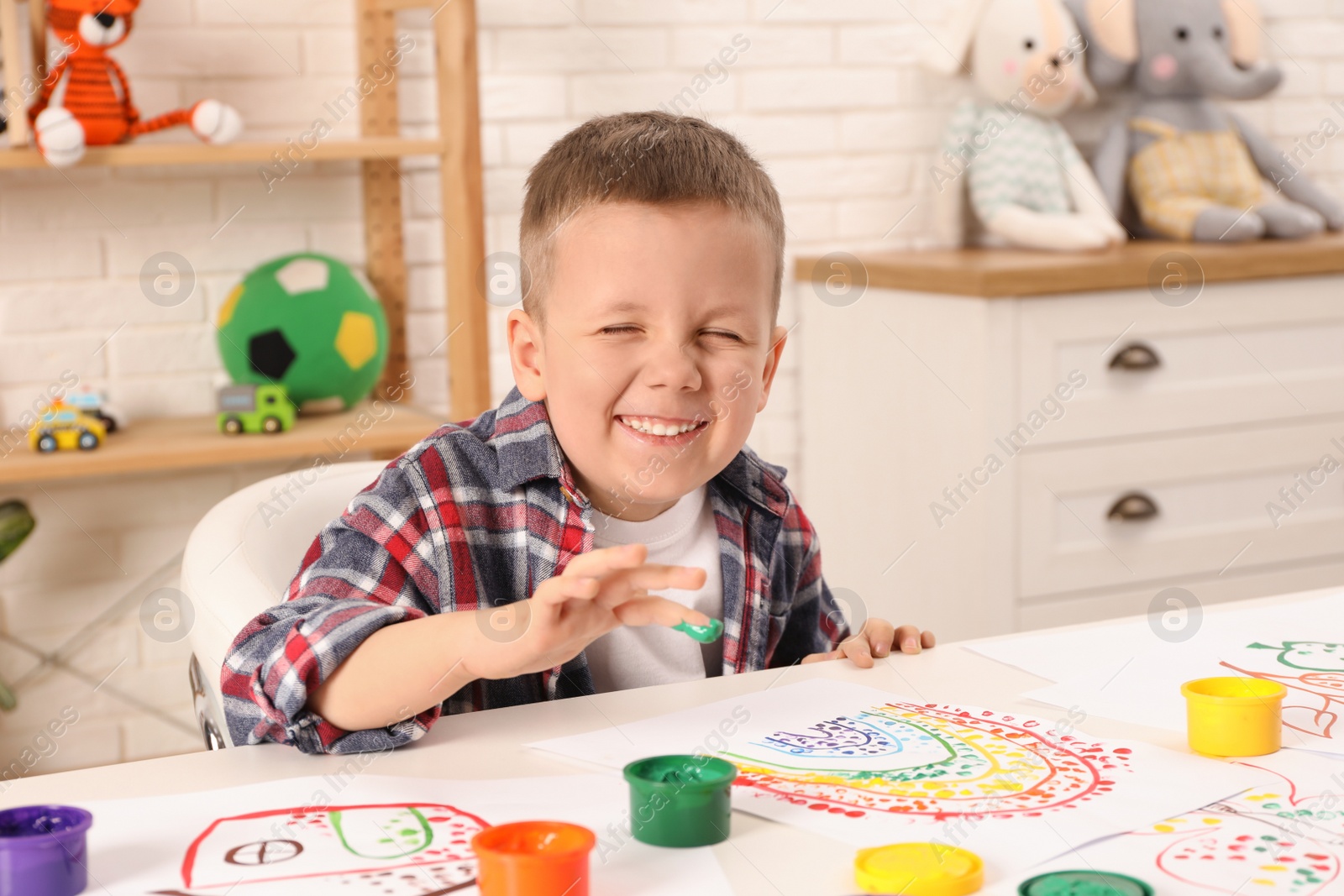 Photo of Little boy painting with finger at white table indoors