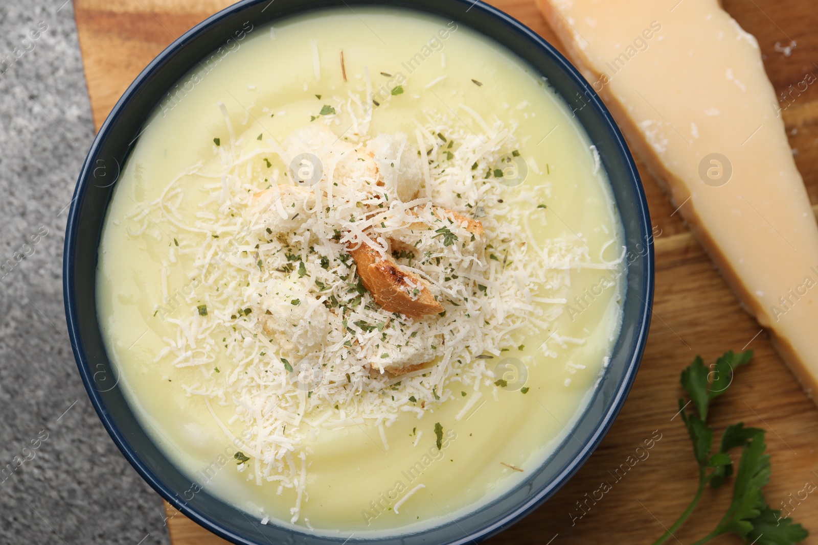 Photo of Delicious cream soup with parmesan cheese and croutons in bowl on grey table, top view