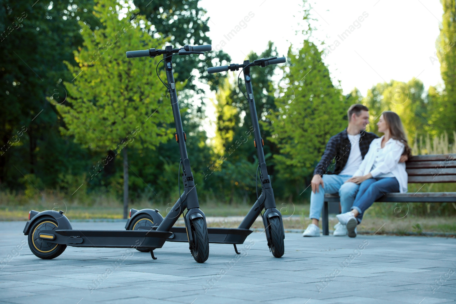 Photo of Modern electric kick scooters and couple spending time together in park, selective focus