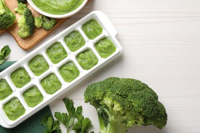 Photo of Broccoli puree in ice cube tray ready for freezing and ingredients on white wooden table, flat lay. Space for text