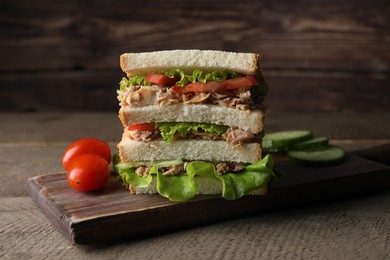 Photo of Delicious sandwich with tuna, tomatoes and lettuce on wooden table