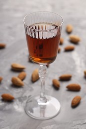 Liqueur glass with tasty amaretto and almonds on light grey table, closeup