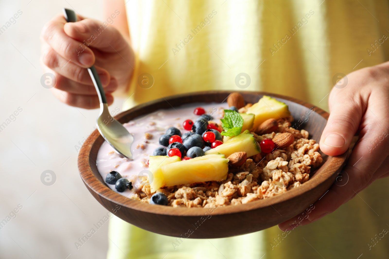 Image of Woman eating tasty granola with yogurt, sliced pineapple and berries for breakfast, closeup