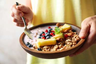 Woman eating tasty granola with yogurt, sliced pineapple and berries for breakfast, closeup