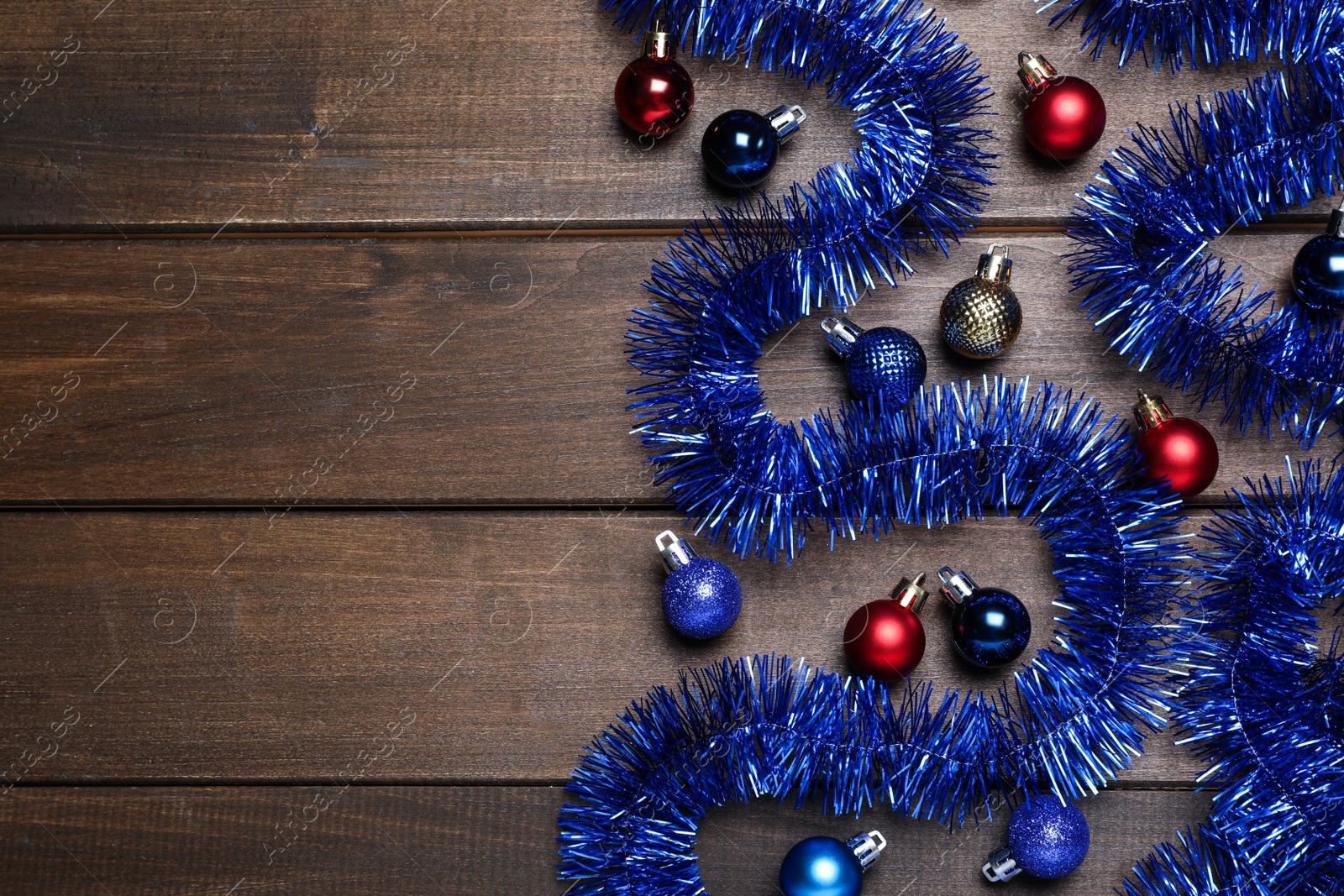 Photo of Bright tinsel and Christmas balls on wooden background, flat lay. Space for text